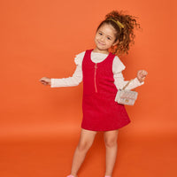 Model can be seen wearing white long sleeve ribbed knit top with ruffles at sleeves paired underneath cherry red sparkly knit jumper. Jumper features a quarter zip zipper and also features pockets at the front. 