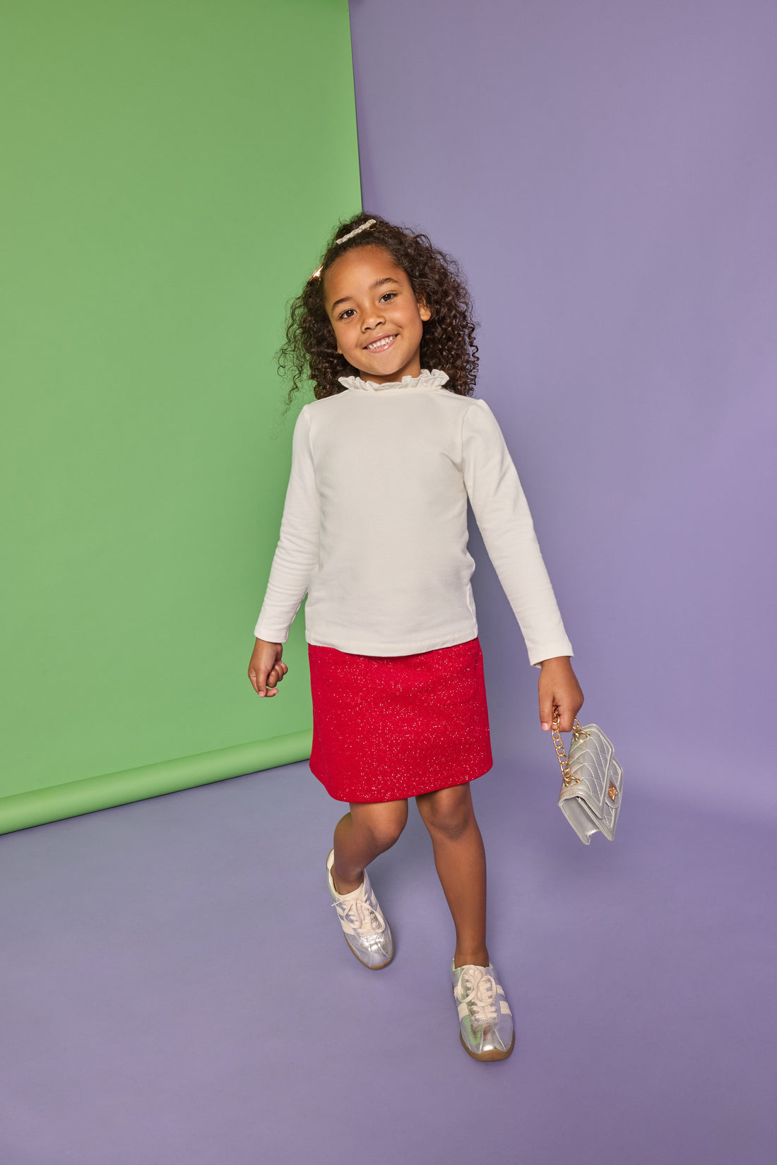 Model can be seen wearing white knit top with high ruffle neckline paired back with a red sparkly fabric knit skort that has pockets on the front. 