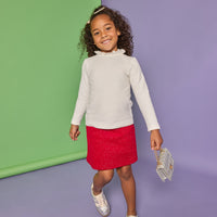 Model can be seen wearing white knit top with high ruffle neckline paired back with a red sparkly fabric knit skort that has pockets on the front. 
