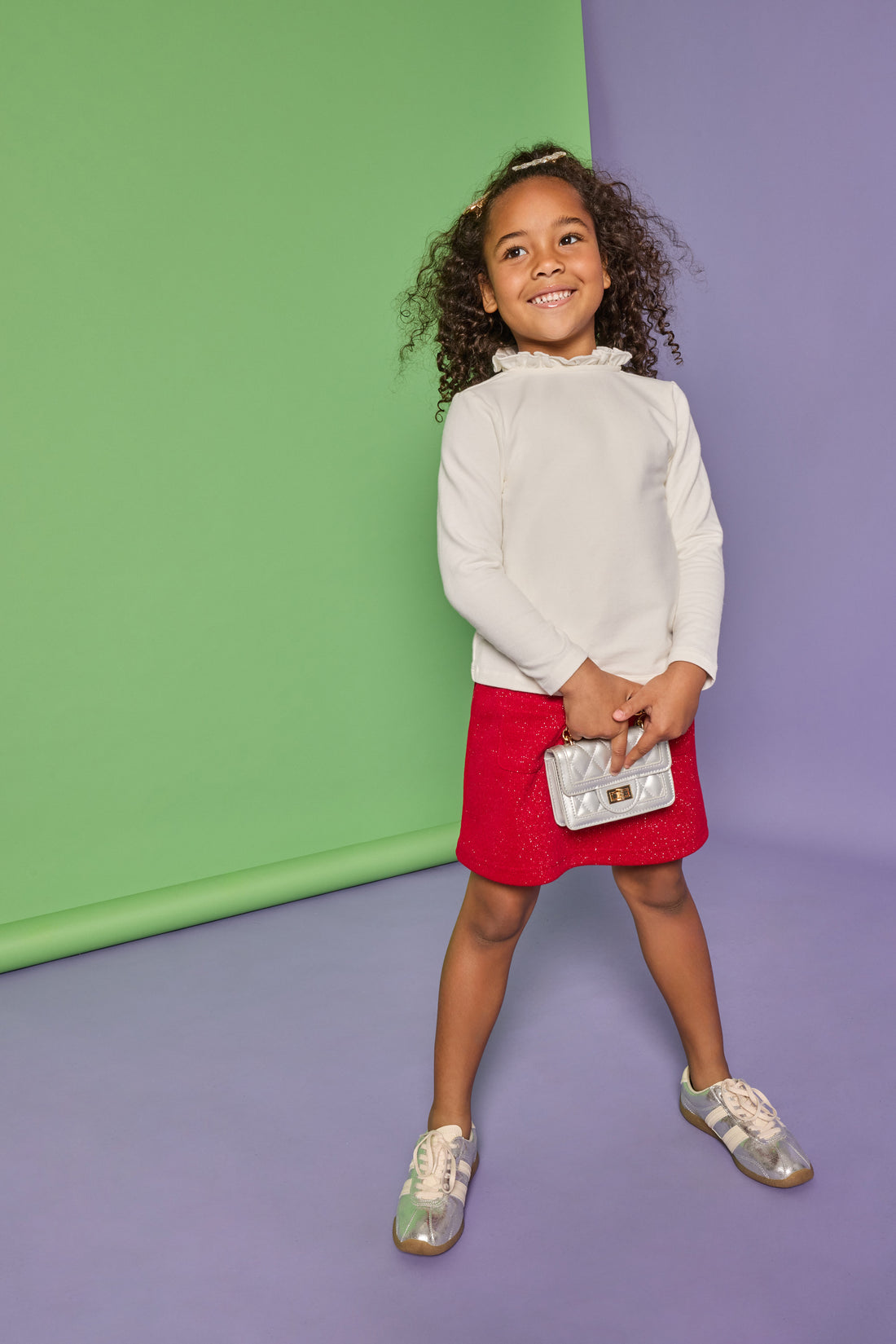 Model can be seen wearing white knit top with high ruffle neckline paired back with a red sparkly fabric knit skort that has pockets on the front. 