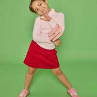 Model can be seen wearing a long sleeve ribbed knit turtleneck in bubblegum pink paired back with a red sparkly knit skort that has two pockets in the front and elastic waistband.
