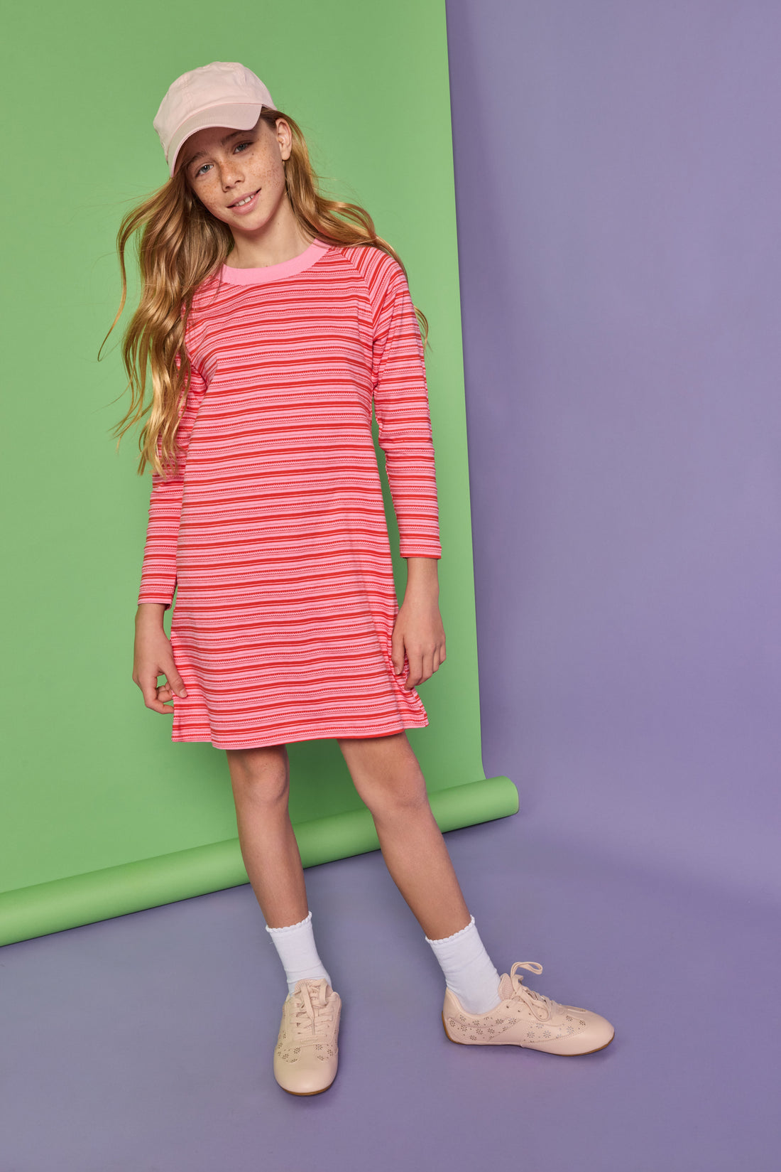 Model can be seen wearing a red and pink stripe knit dress. Dress features a thick pink neckline for an elevated look. 