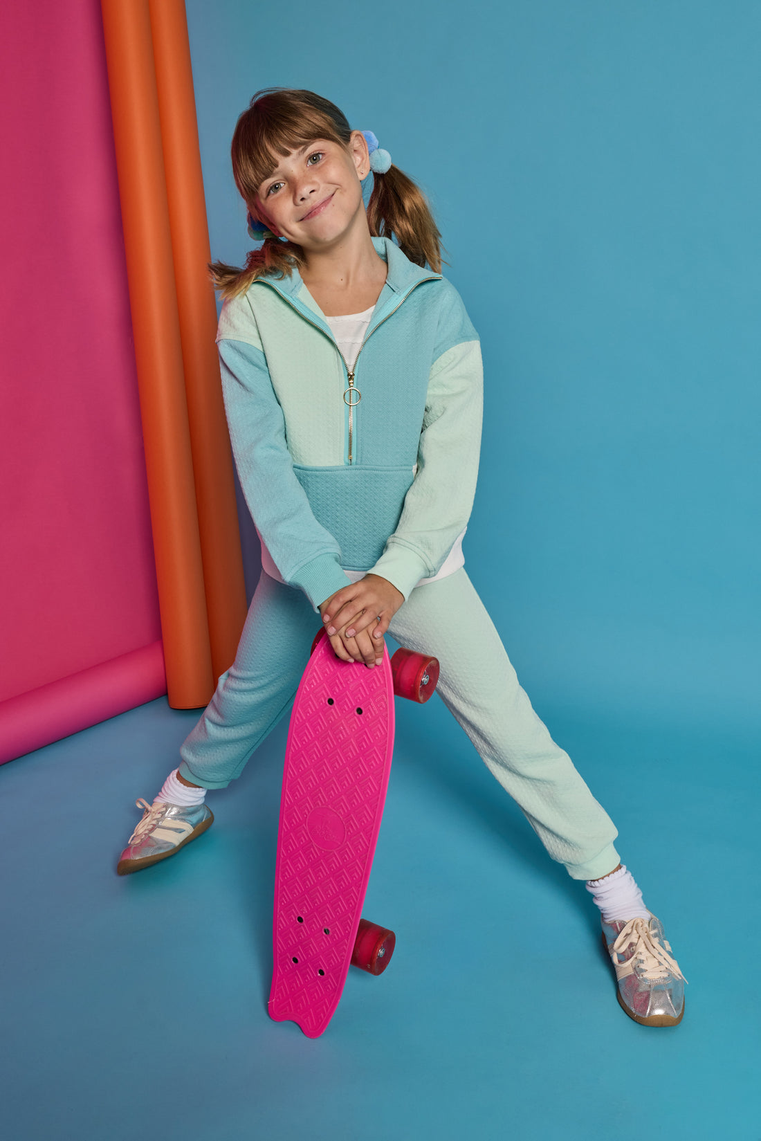 Model can be seen wearing a knit color block set in a teal and light green color. Pullover top features a quarter zip zipper and front pocket. Joggers have on pant leg in the aqua and one in the light green color for an elevated look. 