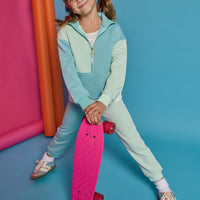 Model can be seen wearing a knit color block set in a teal and light green color. Pullover top features a quarter zip zipper and front pocket. Joggers have on pant leg in the aqua and one in the light green color for an elevated look. 