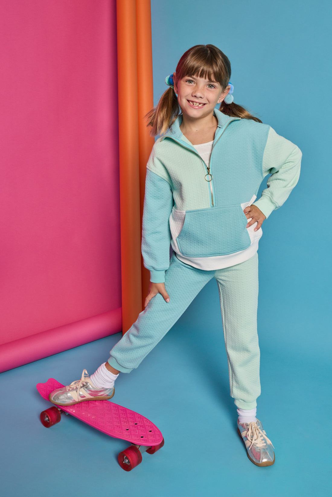 Model can be seen wearing a knit color block set in a teal and light green color. Pullover top features a quarter zip zipper and front pocket. Joggers have on pant leg in the aqua and one in the light green color for an elevated look. 