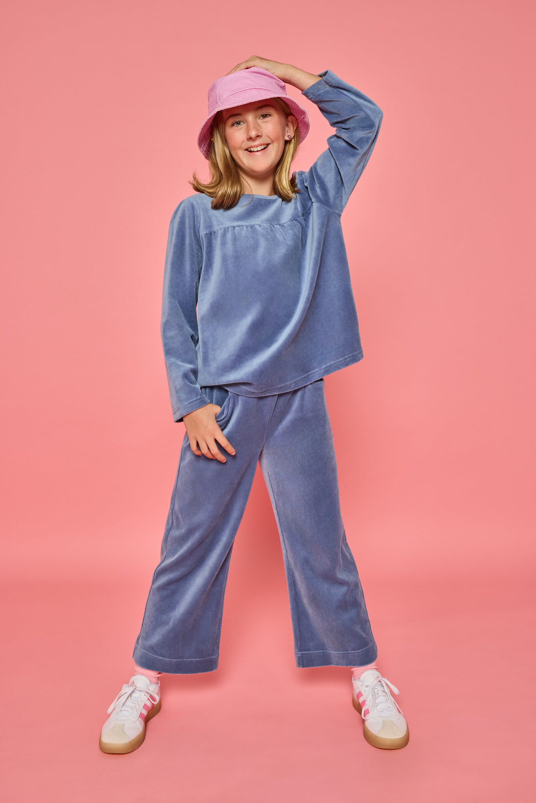 Model can be seen wearing a matching dusty blue velour set. Long sleeve top features button closure at back and pants feature pockets and an elastic waistband for a relaxed but secure fit. 