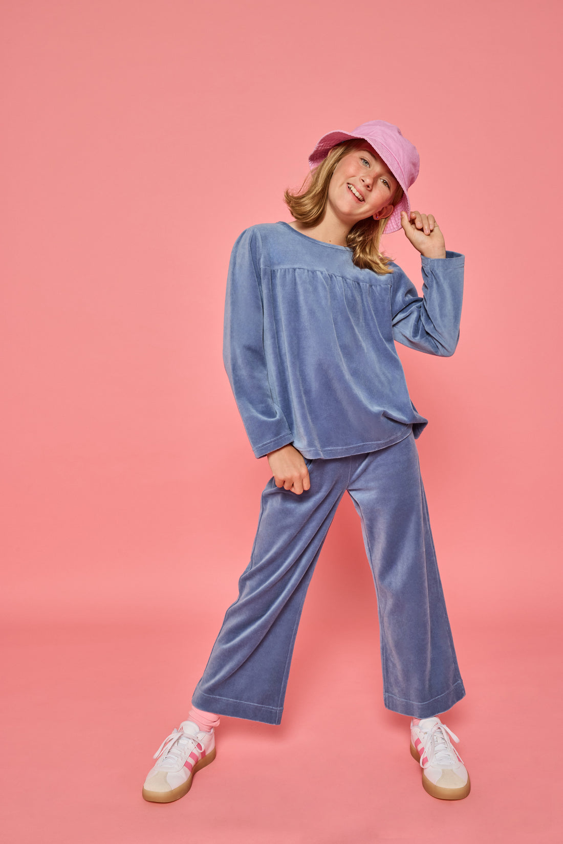 Model can be seen wearing a matching dusty blue velour set. Long sleeve top features button closure at back and pants feature pockets and an elastic waistband for a relaxed but secure fit. 