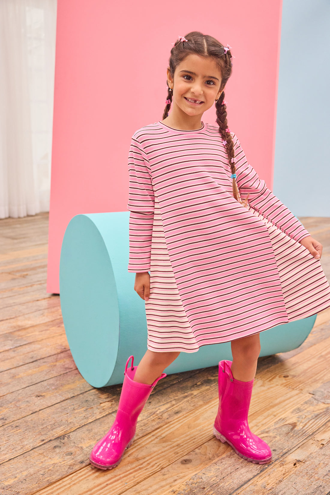 Model can be seen wearing a thicker knit long sleeve dress that features a mixed stripe detail in a magenta/pink/white pattern.