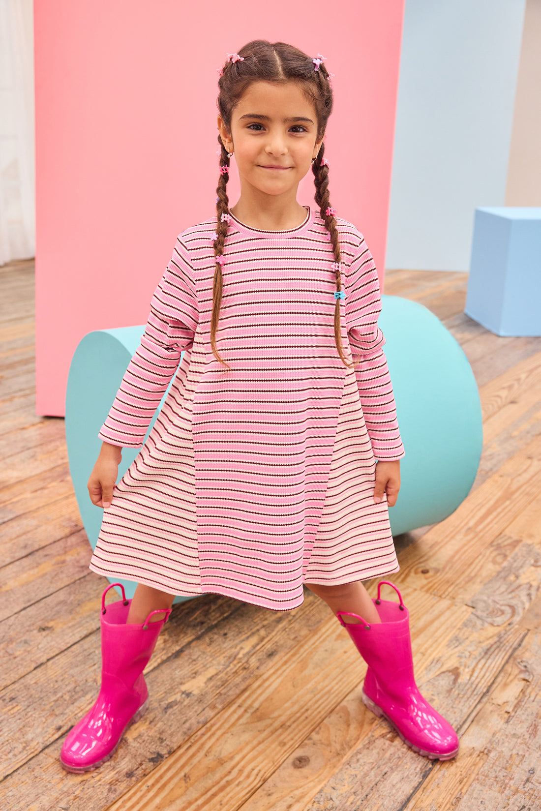 Model can be seen wearing a thicker knit long sleeve dress that features a mixed stripe detail in a magenta/pink/white pattern.
