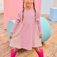Model can be seen wearing a thicker knit long sleeve dress that features a mixed stripe detail in a magenta/pink/white pattern.