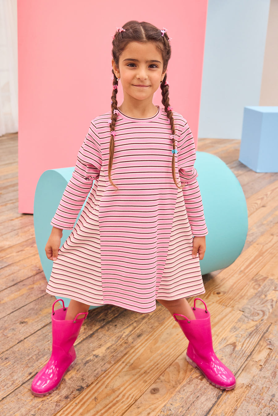 Model can be seen wearing a thicker knit long sleeve dress that features a mixed stripe detail in a magenta/pink/white pattern.