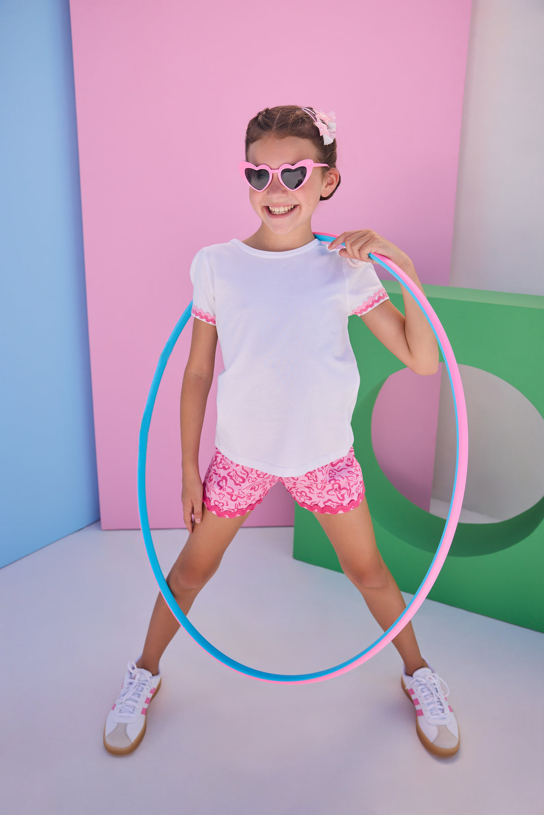 Tween model can be seen wearing a pair of woven hot pink/light pink floral print shorts that feature a ric rac hot pink detail along hem of shorts and an elastic waistband for a comfy but secure fit. Model can also be seen wearing a white tee with the same color light pink/hot pink ric rac detail at bottom of sleeves to complete the look. 