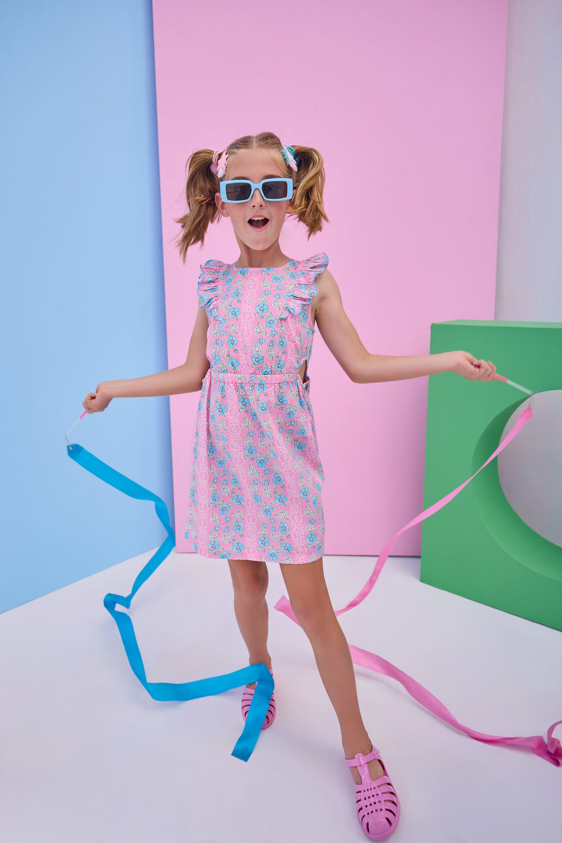 Model can be seen wearing a woven pink/light blue floral dress that features two cutout features on the sides of the dress to give it an elevated/big girl feel. 