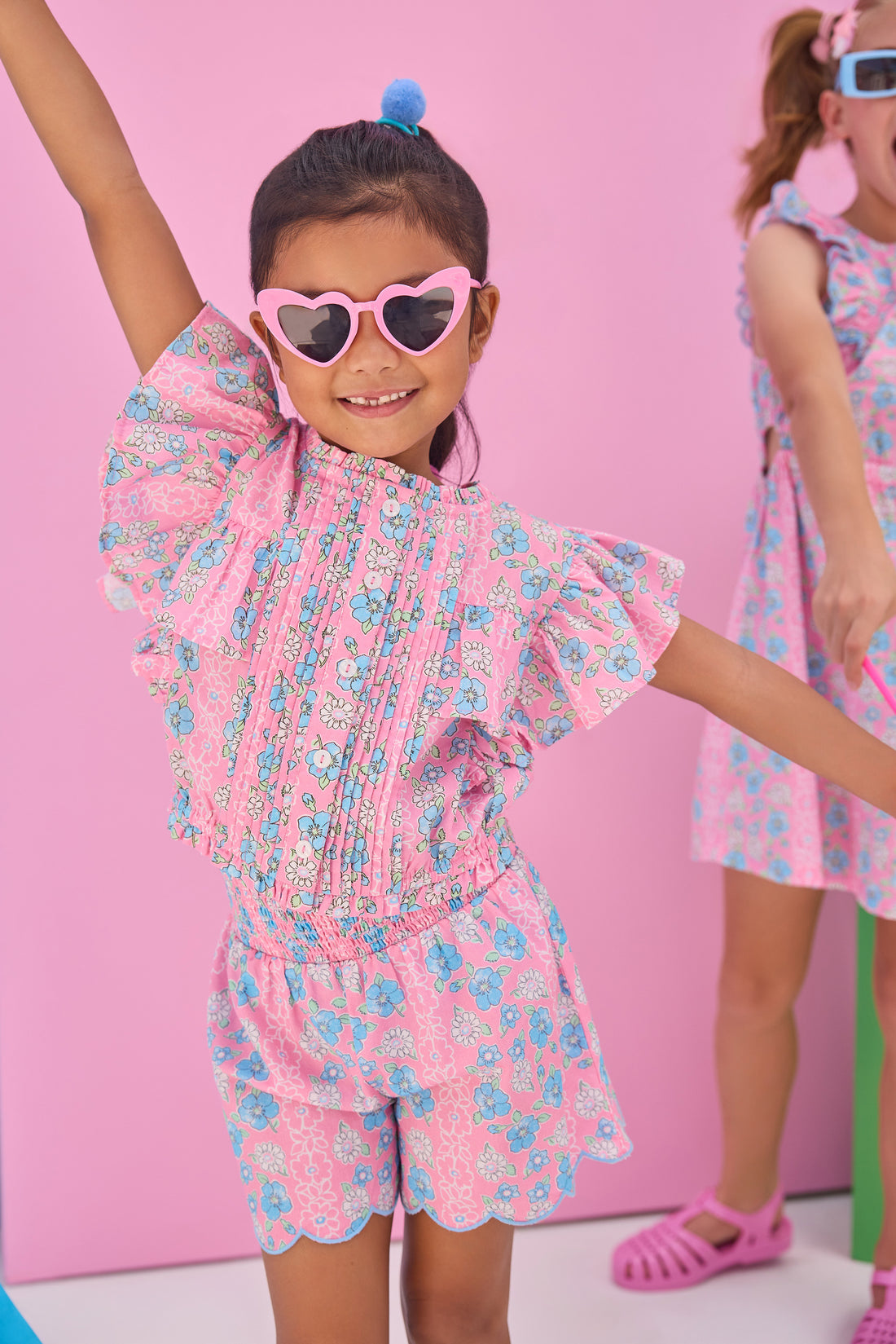 Model can be seen wearing shirred shorts in a pink/blue floral print. Shorts feature smocking along waist and scallop edges to elevate the look. Shorts pair back perfectly with woven top in matching floral print to complete the look. 
