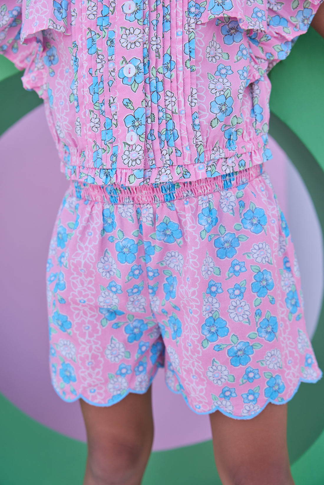 Model can be seen wearing a woven pink and blue floral top that features button closures along the front and big angel sleeve detail to elevate the look. Top pairs back perfectly with the shirred shorts in the same matching print to complete the look. 