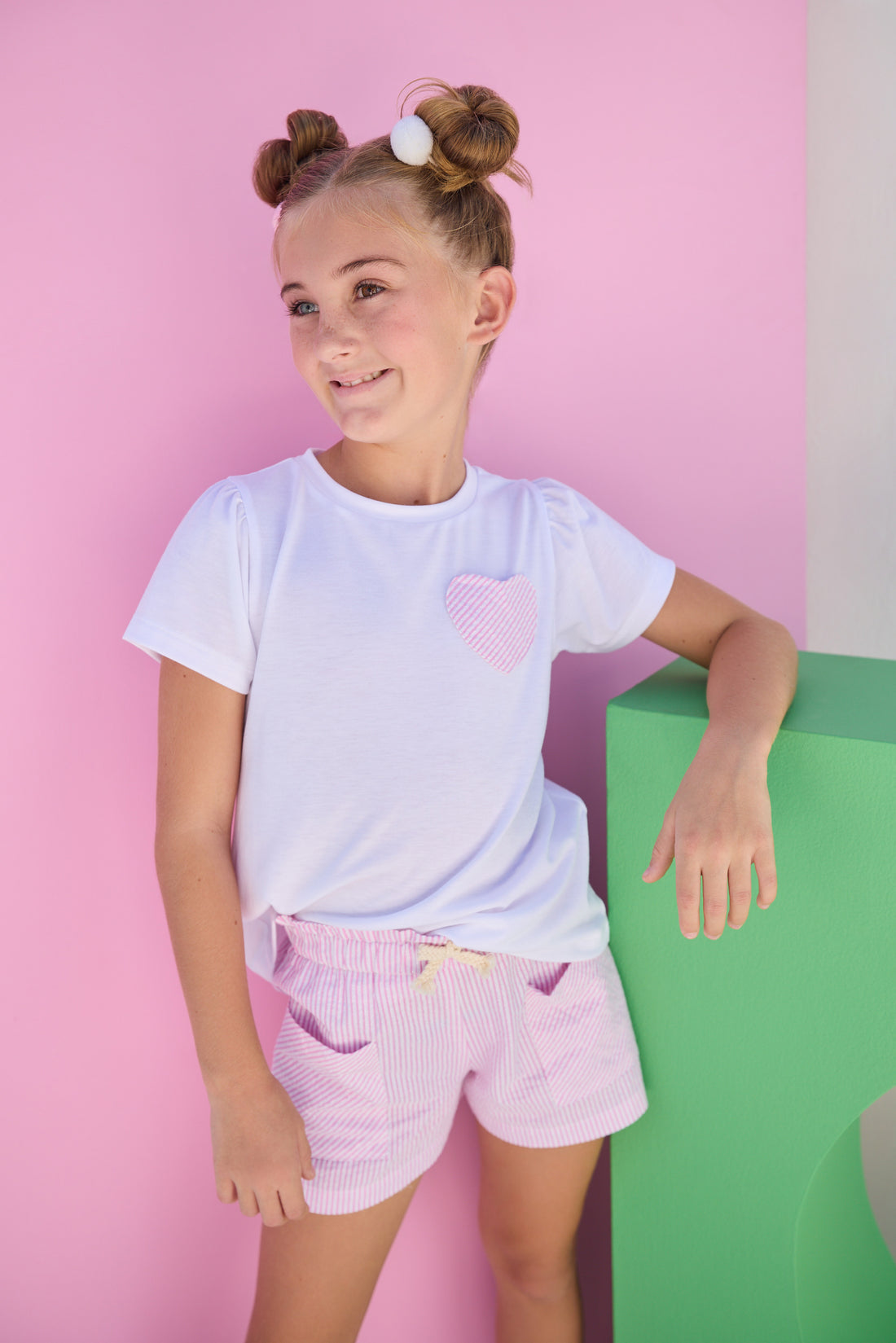 Tween model can be seen wearing pink sparkly seersucker woven shorts that feature an elastic waistband and two pockets in the front. Shorts pair back perfectly with basic white tee with faux heart pocket in the same pink seersucker fabric to complete the look. 
