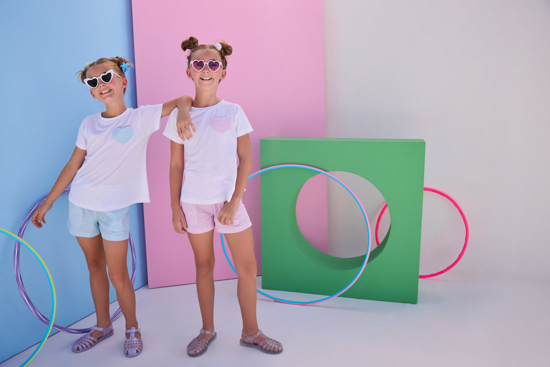 Model on left can be seen wearing woven seersucker sparkly blue shorts that feature two pockets in front and an elastic waistband. Shorts pair back perfectly with matching white tee that has the same sparkly blue seersucker fabric on the faux heart pocket to complete the look.