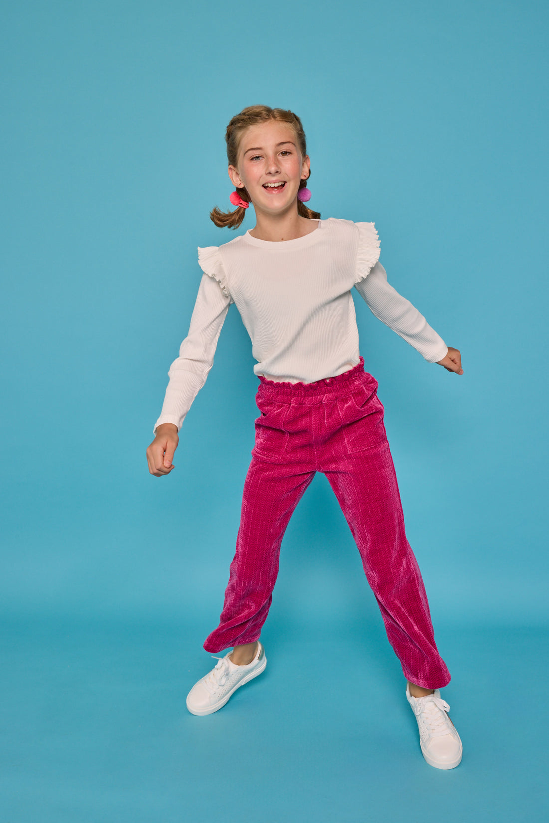 Model can be seen wearing fuchsia herringbone corduroy pants that feature pockets and an elastic waistband. Paired back with the white ribbed ruffle sleeve long sleeve shirt to complete the look. 