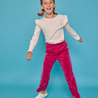 Model can be seen wearing fuchsia herringbone corduroy pants that feature pockets and an elastic waistband. Paired back with the white ribbed ruffle sleeve long sleeve shirt to complete the look. 