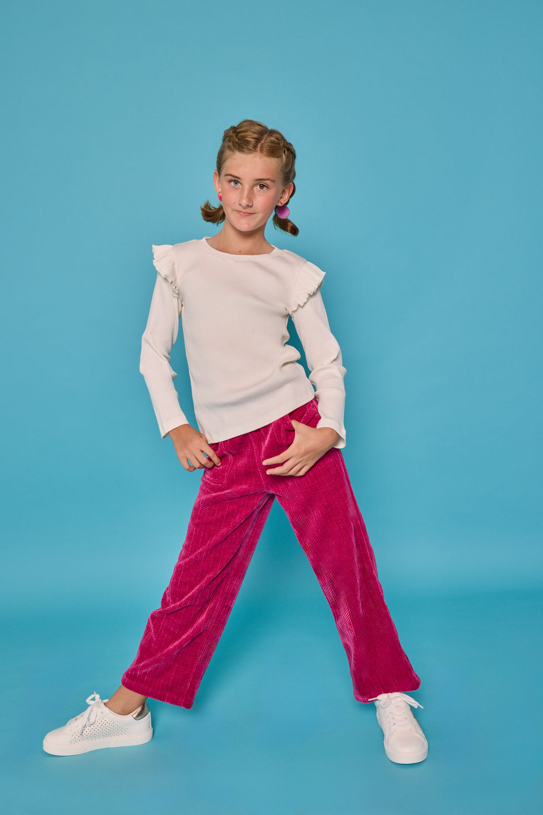 Model can be seen wearing fuchsia herringbone corduroy pants that feature pockets and an elastic waistband. Paired back with the white ribbed ruffle sleeve long sleeve shirt to complete the look. 