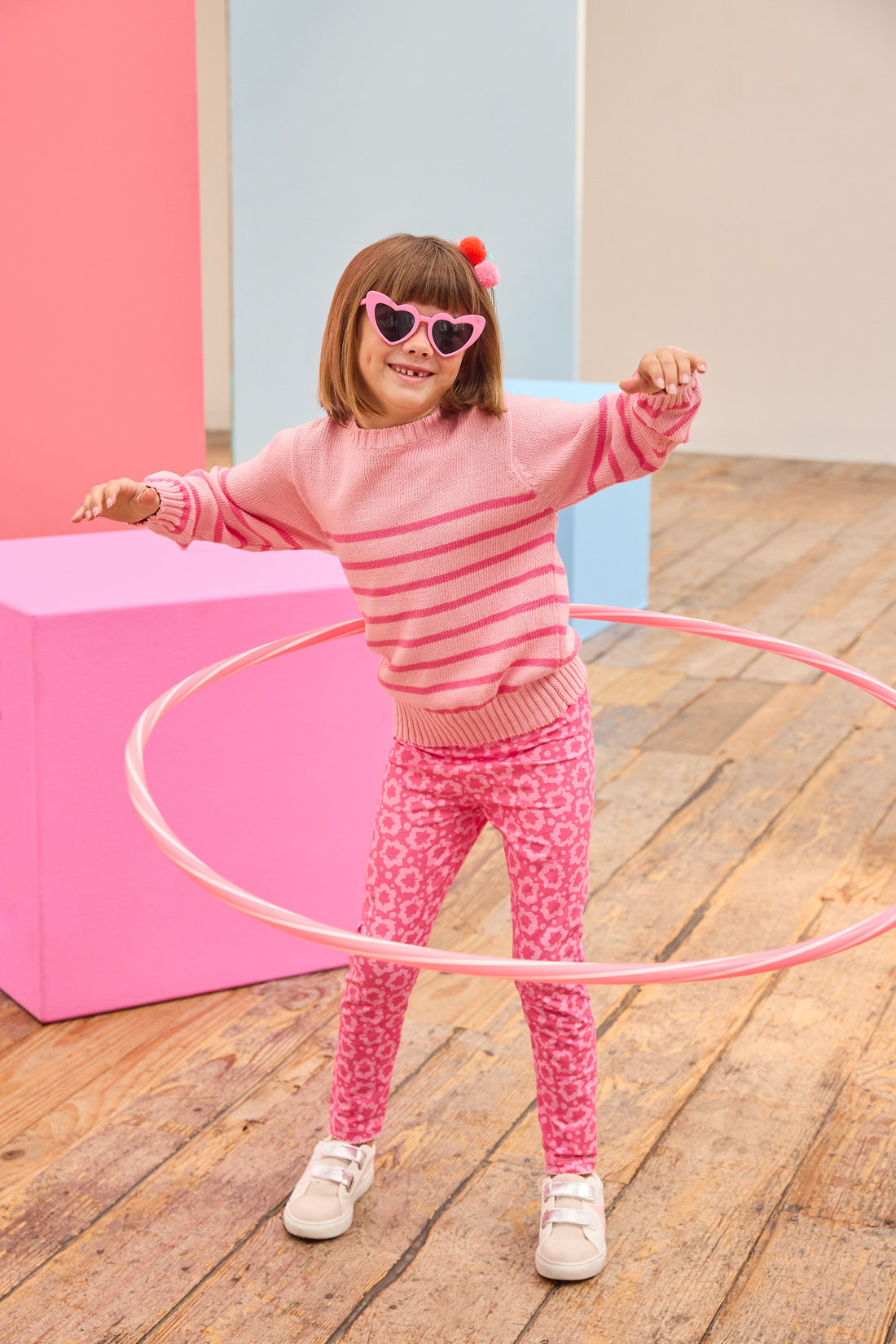 Child in pink sweater and leggings with hula hoop on wooden floor