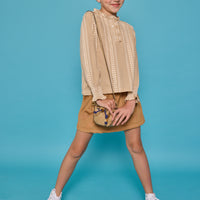 Model can be seen wearing a long sleeve woven top in a tan/cream  print. Top features button closure packet down bust and smocking detail at sleeves for an elevated look. Paired back with our brown faux suede skort that has built in shorts and pocket detail at front. 