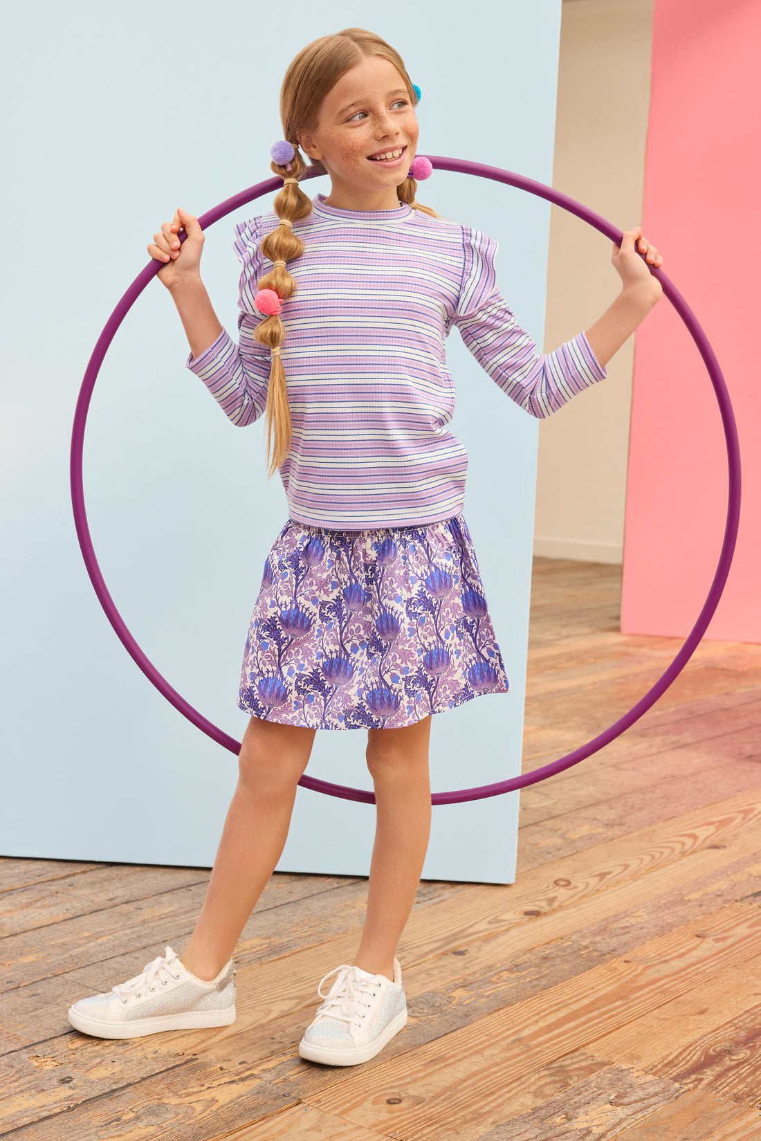 Model can be seen wearing blue/purple/white floral skort that features elastic ruching at the waist and built in shorts for a secure fit. Skort pairs back perfectly with striped ribbed top in purple/white/blue stripes. 