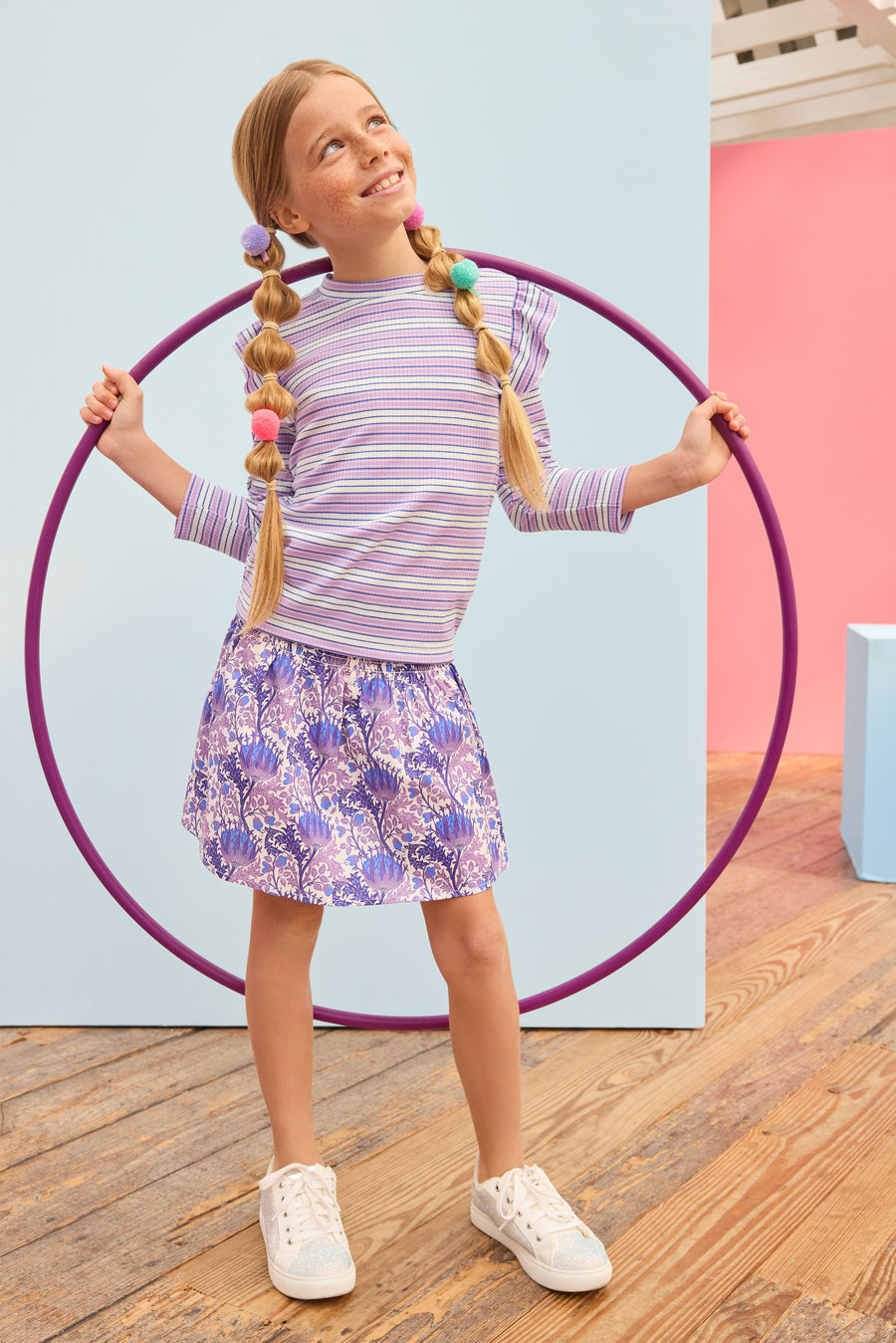 Model can be seen wearing blue/purple/white floral skort that features elastic ruching at the waist and built in shorts for a secure fit. Skort pairs back perfectly with striped ribbed top in purple/white/blue stripes. 