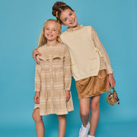 Model on the right can be seen wearing tan/cream pattern woven top paired underneath a cream sweater vest with ties at sides for an elevated look. Paired back with our skort in brown faux suede to complete the look. Model on the left can be seen wearing the matching print in a woven dress with buttons down the front and ruffles at bust for an elevated look. 