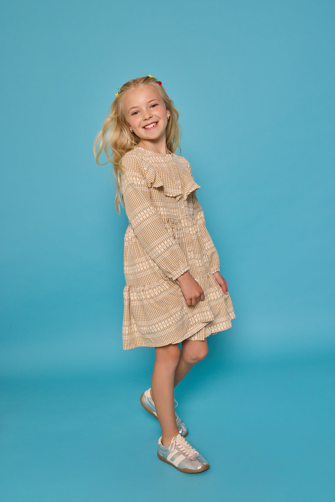 Model can be seen wearing long sleeve woven khaki gingham dress. Dress features buttons down the front and a ruffle at the bodice for an elevated look. 