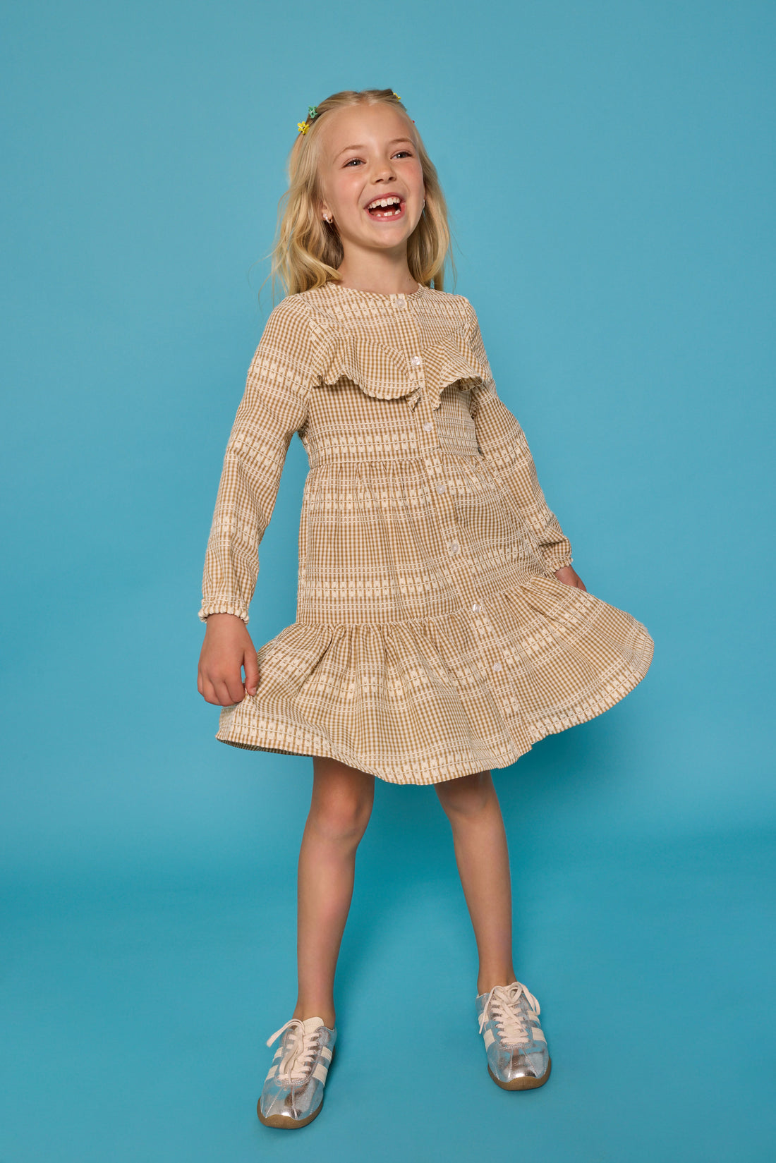 Model can be seen wearing long sleeve woven khaki gingham dress. Dress features buttons down the front and a ruffle at the bodice for an elevated look. 