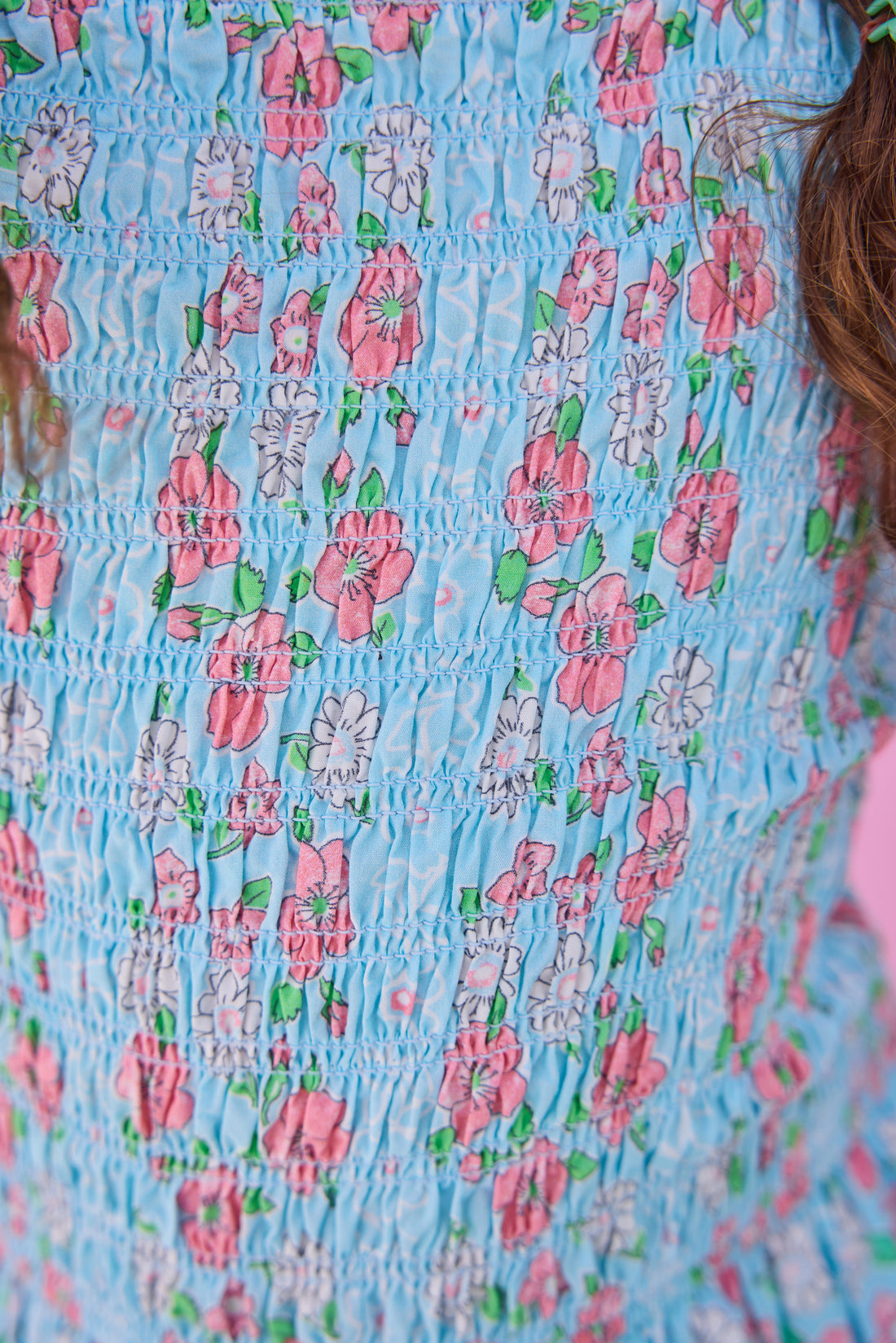 Model can be seen wearing woven pink and aqua floral print top that features elastic smocking throughout the body of the top for a stretchy but secure fit. 