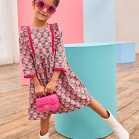 Model can be seen wearing pink/green/green floral pattern woven dress that features velour detail along bottoms of sleeves and trim of chest ruffle detail for an elevated look.