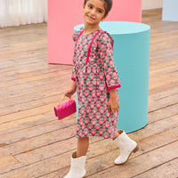 Model can be seen wearing pink/green/green floral pattern woven dress that features velour detail along bottoms of sleeves and trim of chest ruffle detail for an elevated look.