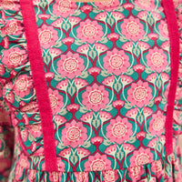 Model can be seen wearing pink/green/green floral pattern woven dress that features velour detail along bottoms of sleeves and trim of chest ruffle detail for an elevated look.
