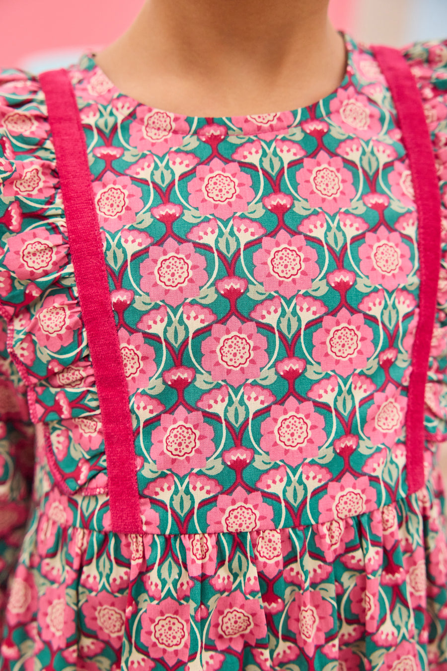 Model can be seen wearing pink/green/green floral pattern woven dress that features velour detail along bottoms of sleeves and trim of chest ruffle detail for an elevated look.