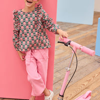 Model can be seen wearing pink/green/dark magenta floral woven top that has ruffle detail down the front of shirt for an elevated look, pairs back perfectly with bubblegum pink twill pants to complete the outfit. 