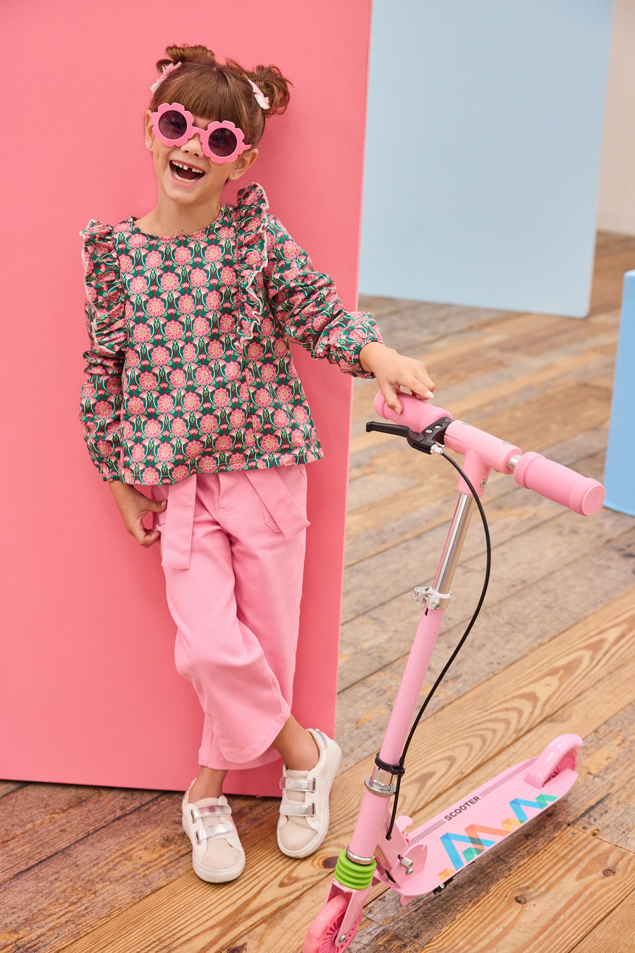Model can be seen wearing pink/green/dark magenta floral woven top that has ruffle detail down the front of shirt for an elevated look, pairs back perfectly with bubblegum pink twill pants to complete the outfit. 