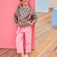 Model can be seen wearing pink/green/dark magenta floral woven top that has ruffle detail down the front of shirt for an elevated look, pairs back perfectly with bubblegum pink twill pants to complete the outfit. 
