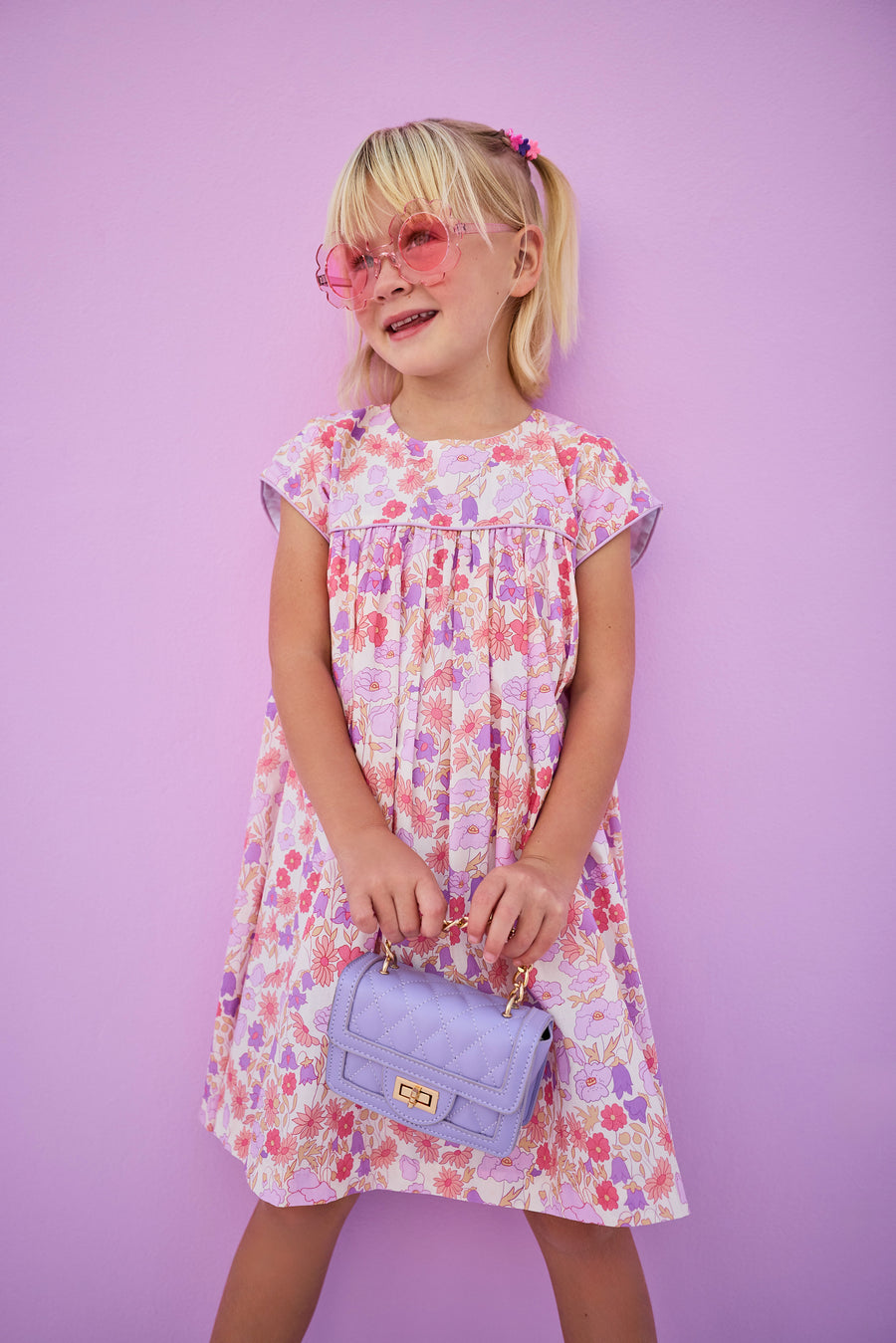 Girls/tween woven dress in a lavender/salmon floral print with matching lavender piping across bust and sleeves. Dress features button closures along back and made of a lightweight material that is lined for a secure but comfy fit. 