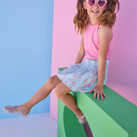 Tween model can be seen wearing a smocked waist woven skirt in a pink and blue floral print. Skirt features smocking detail at waist for a secure but comfy fit. Skirt pairs back perfectly with a hot pink halter top that has button closures along back. 