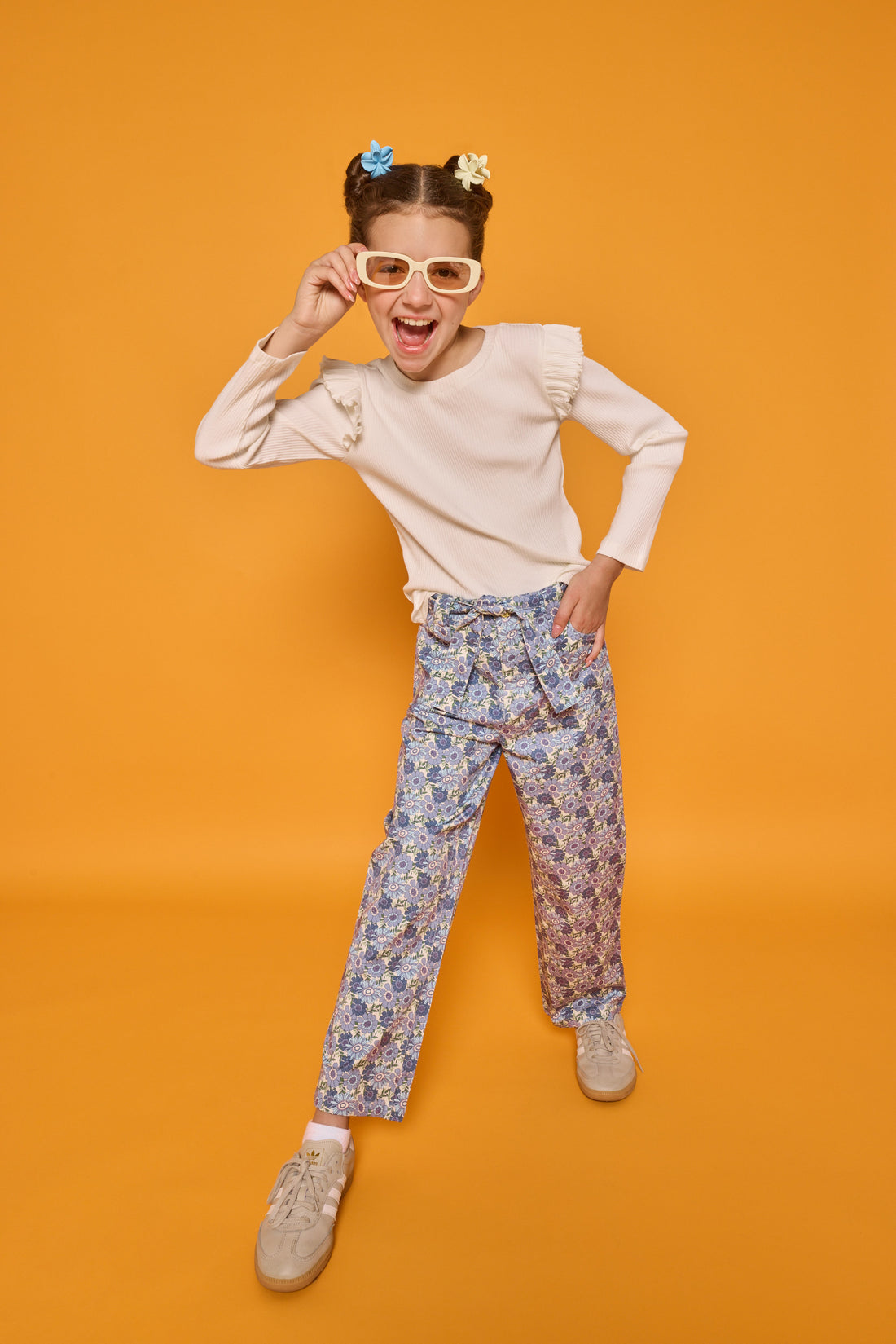 Model can be seen wearing cream/white ribbed knit long sleeve top with ruffle detail at sleeves paired back with corduroy pants in a blue floral print. Pant features belt and belt loops that also come with the pant. 