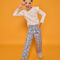 Model can be seen wearing cream/white ribbed knit long sleeve top with ruffle detail at sleeves paired back with corduroy pants in a blue floral print. Pant features belt and belt loops that also come with the pant. 