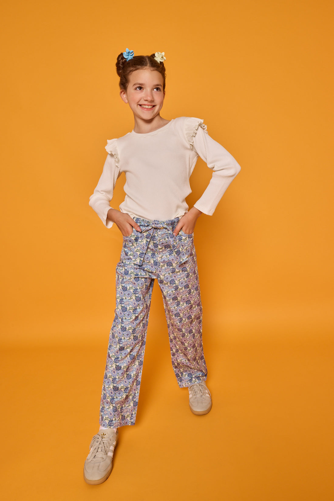Model can be seen wearing cream/white ribbed knit long sleeve top with ruffle detail at sleeves paired back with corduroy pants in a blue floral print. Pant features belt and belt loops that also come with the pant. 
