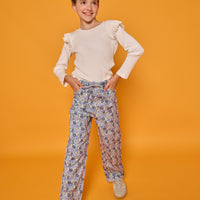 Model can be seen wearing cream/white ribbed knit long sleeve top with ruffle detail at sleeves paired back with corduroy pants in a blue floral print. Pant features belt and belt loops that also come with the pant. 