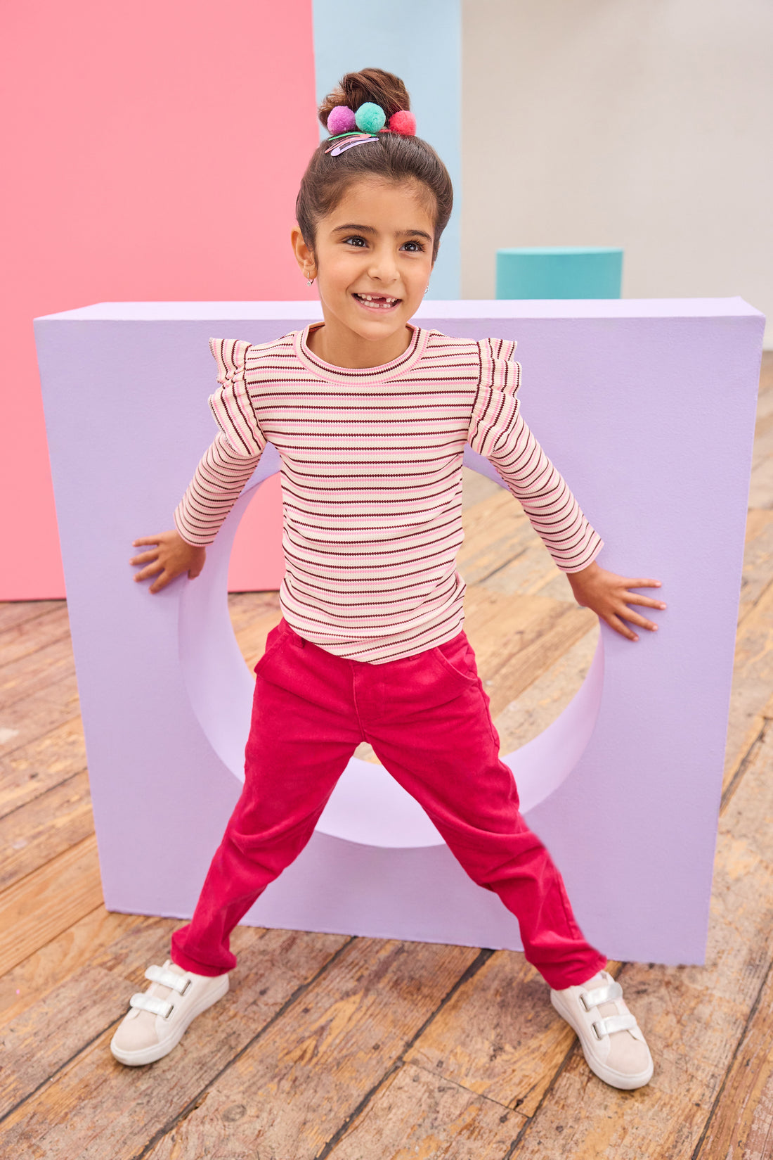 Model can be seen wearing a soft striped knit long sleeve shirt in a pink/maroon/cream stripe. Top features ruffle/angle sleeve detail to elevate the look. Pairs back perfectly with cranberry color velvet pants to complete the look. 