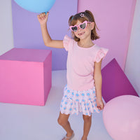 Model can be seen wearing two tiered skort in a blue/red/pink pattern that features scallop edges in pink embroidery, built in shorts, and an elastic waistband. Skort pairs back perfectly with the knit light pink top that features an eyelet detail on the angel sleeves to complete the look. 