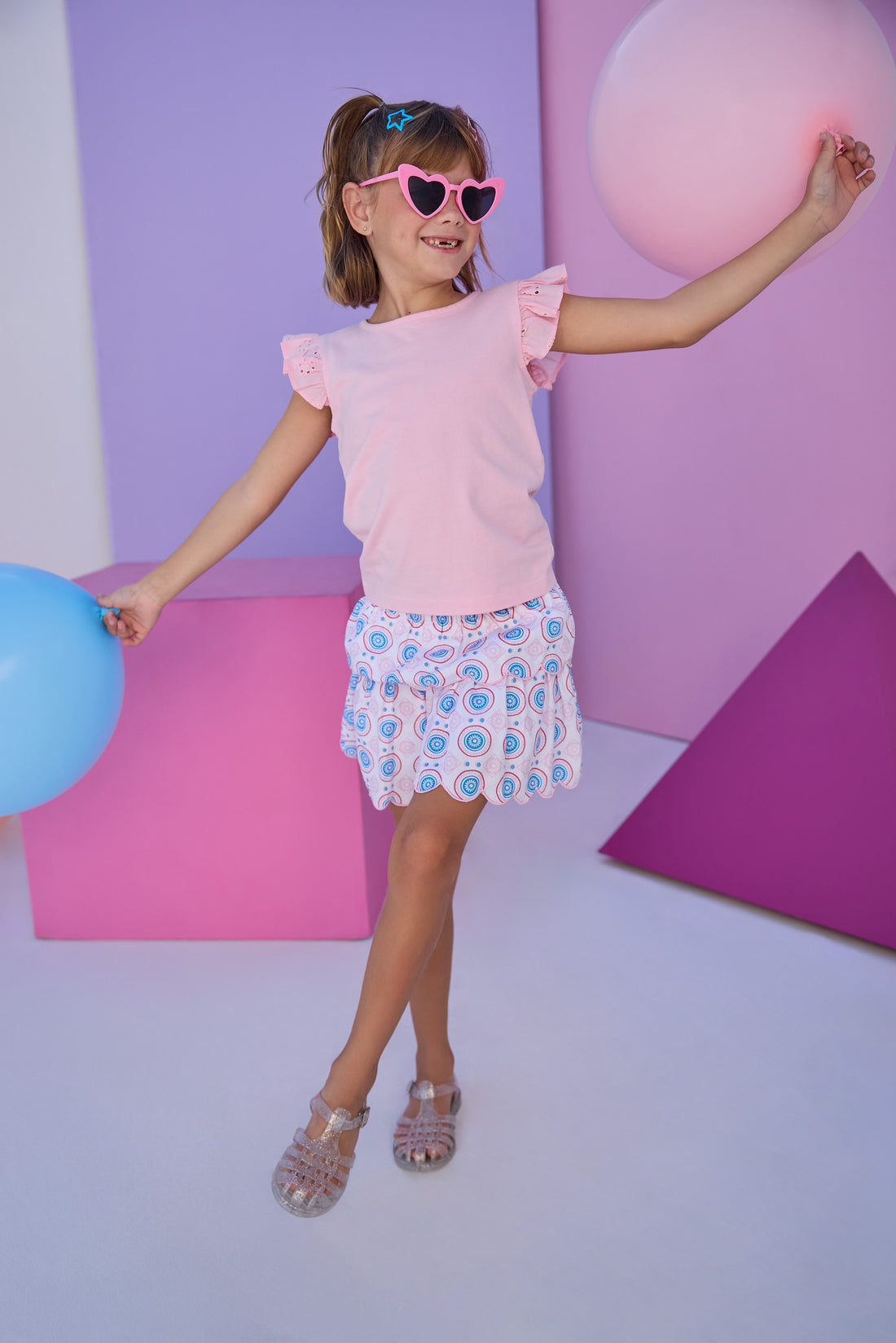 Model can be seen wearing a light pink knit short sleeve top that features eyelet detail on the angel sleeves. Top can be paired back with many bottoms in the line, as it is a solid pink shirt, easy to mix and match. 