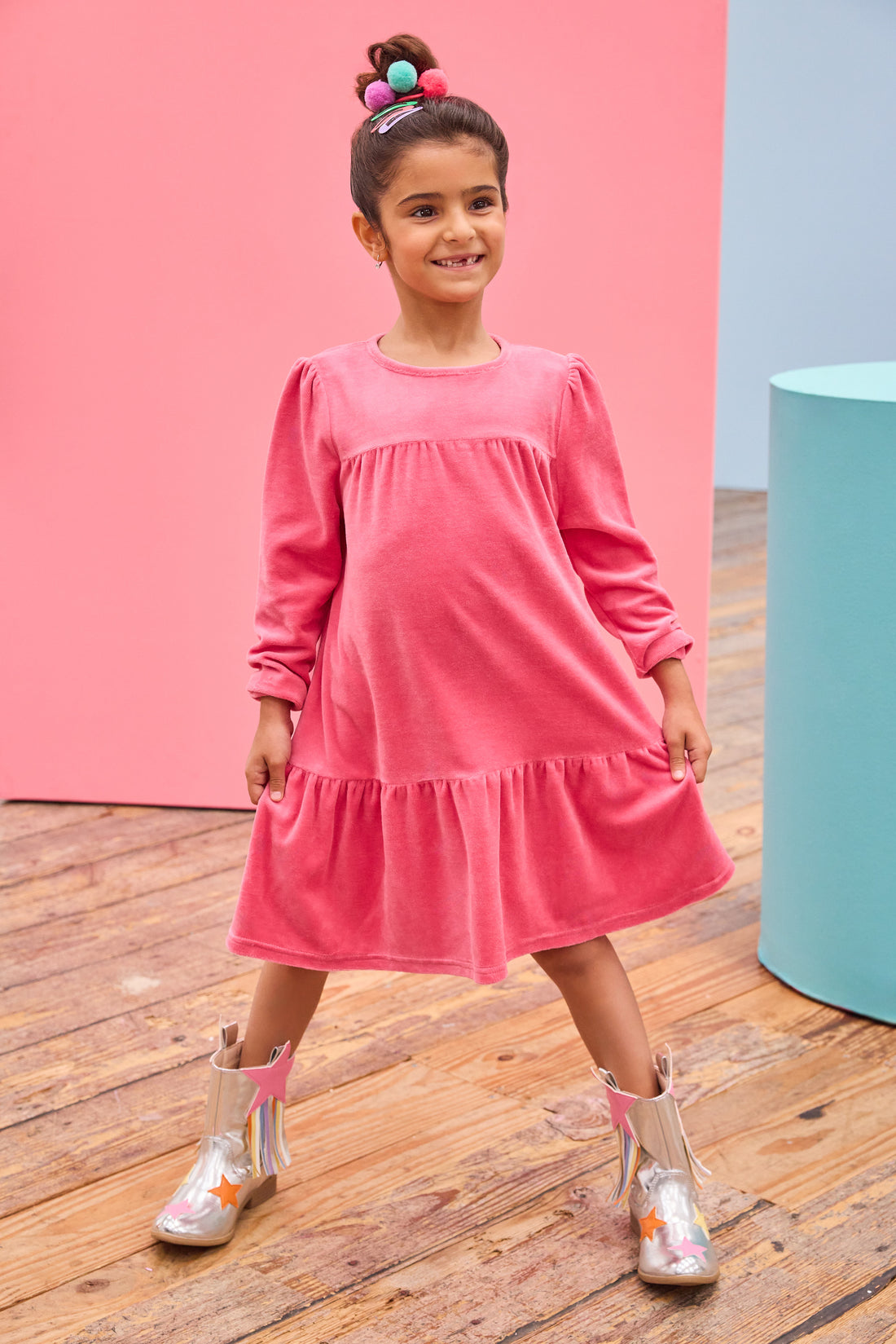 - [ ] Model can be seen wearing long sleeve velour dress in periwinkle blue. Dress features button closure at back, and pleating detail across bust and bottom tier of dress for an elevated look. 