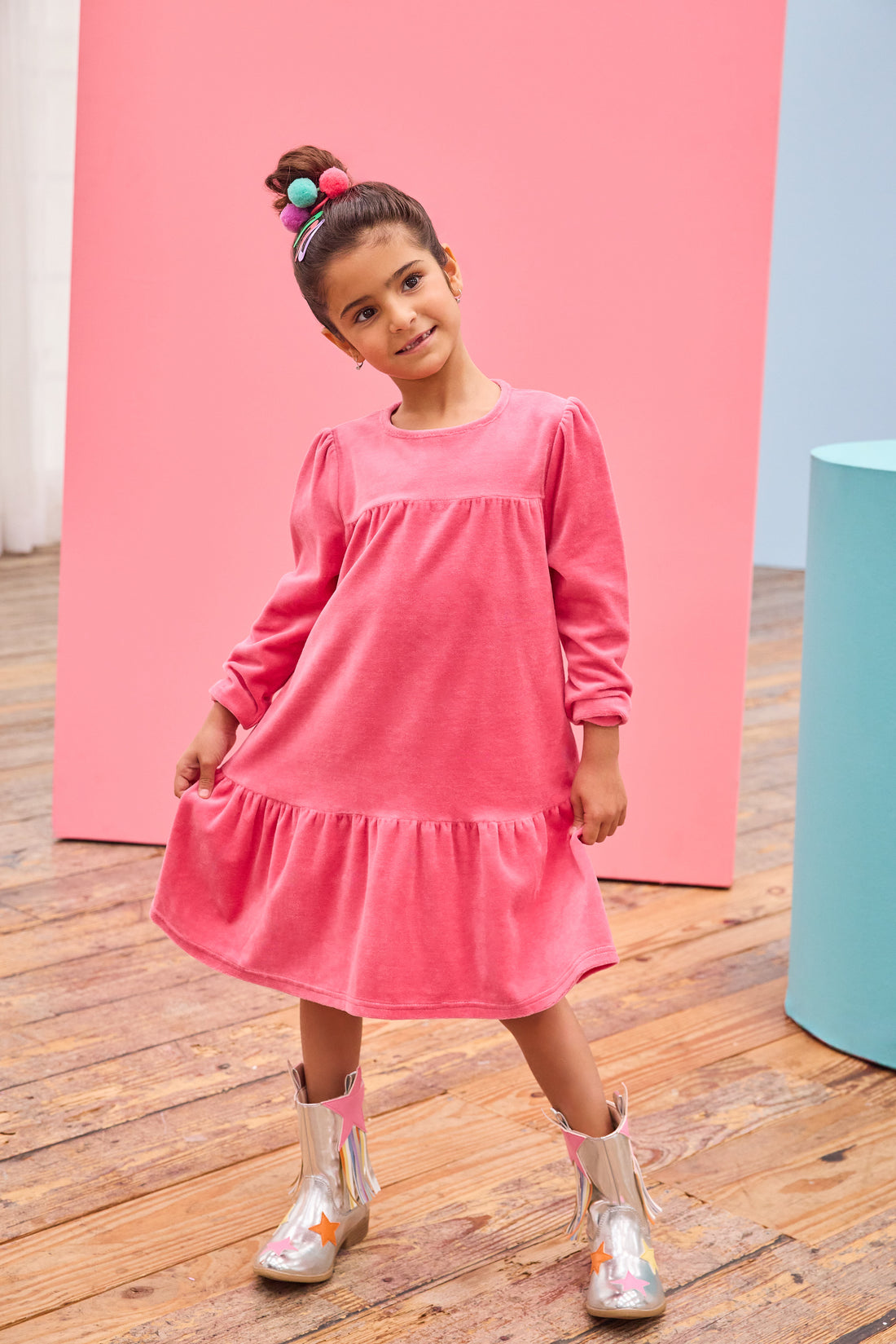 - [ ] Model can be seen wearing long sleeve velour dress in periwinkle blue. Dress features button closure at back, and pleating detail across bust and bottom tier of dress for an elevated look. 